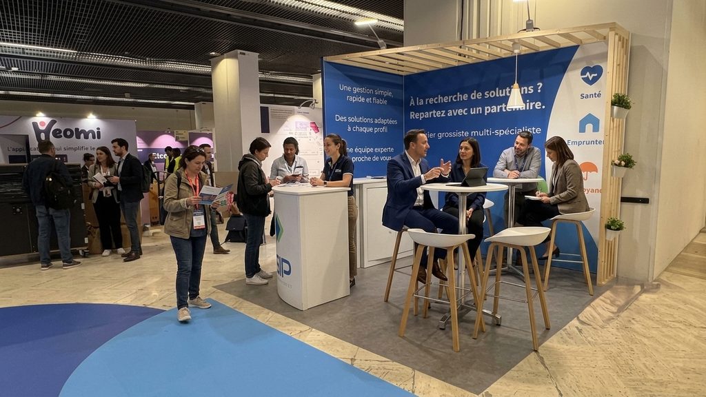 Stand Néoliane UGIP aux Journées du Courtage Paris 2026 — comptoir rond double branding et coin salon discussion du stand